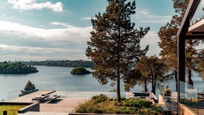 A modern outdoor deck with seating, a view of a lake, and a cityscape in the background. - Most Luxurious 5-bed Villa in Boo Stockholm (Värmdö)
