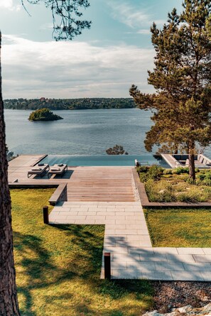 Una terraza a la orilla del lago con sillones, un muelle de madera y vistas a un lago y una isla distante.