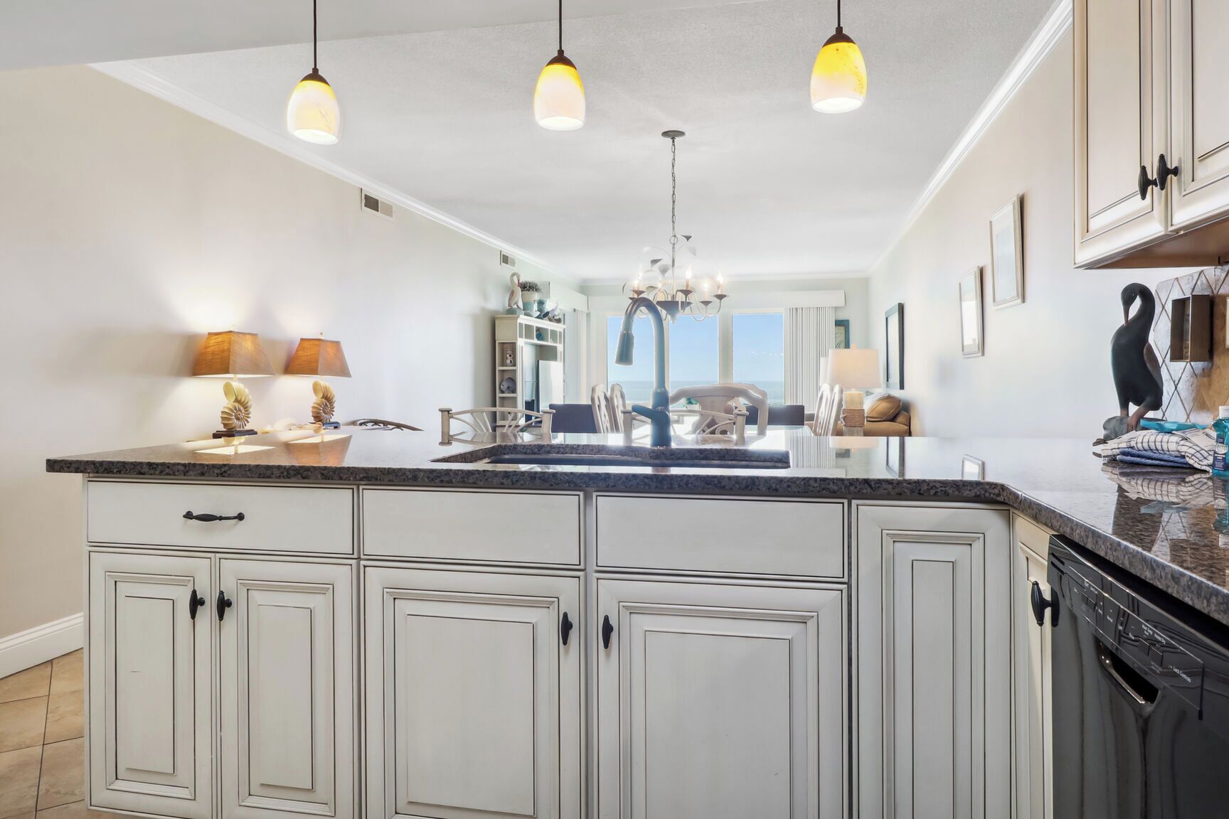 A kitchen with a large island, white cabinetry, pendant lighting, and a view of the ocean.