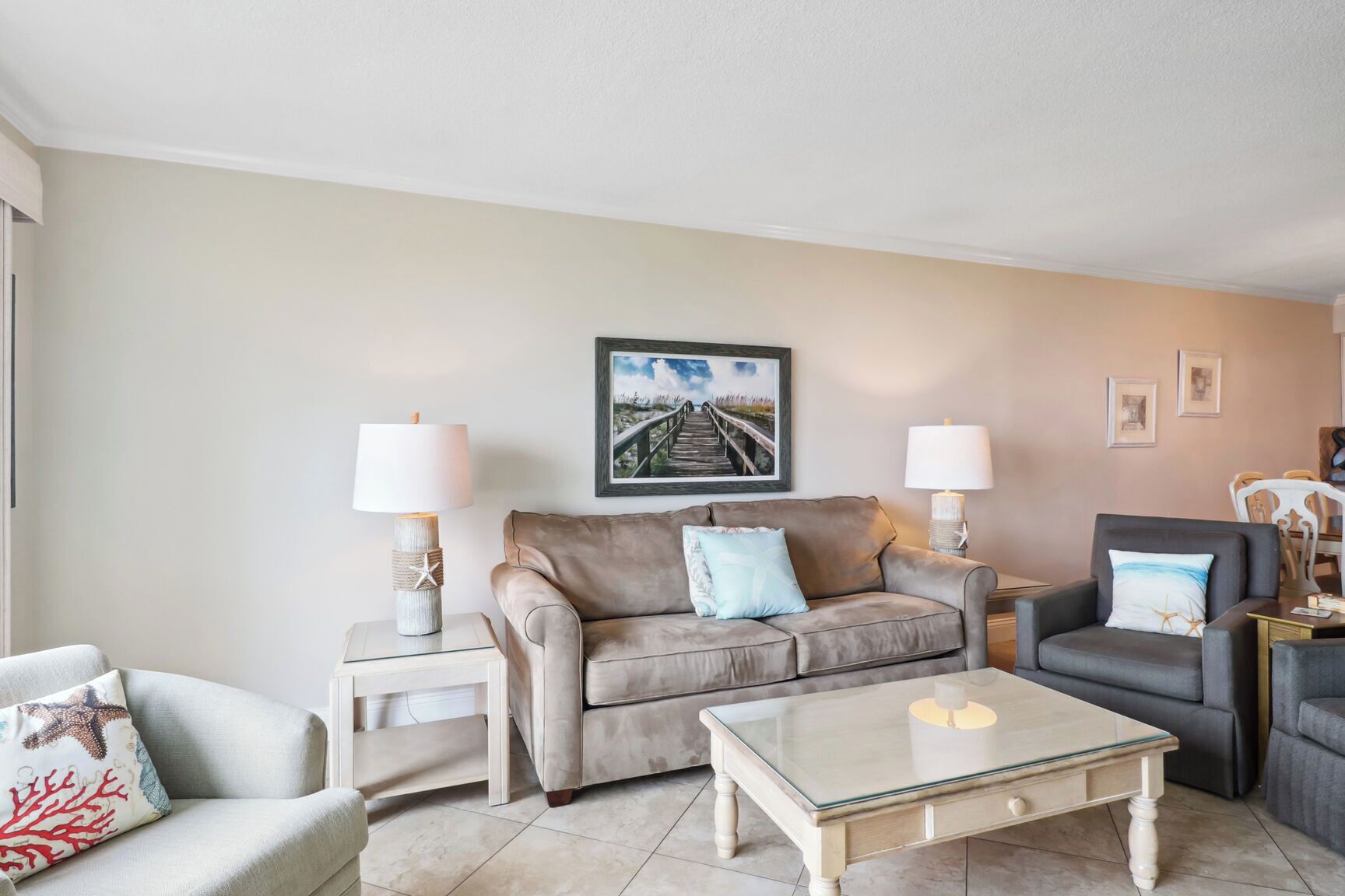 A living room with a beige sofa, two side tables with lamps, a glass coffee table, and a framed picture on the wall.