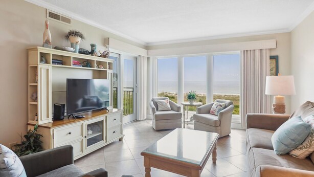 A spacious living room with a flat-screen TV, comfortable seating, a glass coffee table, and a view of the beach through large windows. - Shorewood 403- Oceanfront 4th Floor Condo (Hilton Head Island)