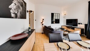 A modern living room with a flat-screen TV, a sofa, a dining table with chairs, and a large abstract painting.