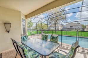 A covered patio with a glass table and chairs, a pool, and a view of houses in the background. - Stunning Home w Private Pool & Spa, Free Waterpark (Kissimmee)