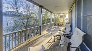 Varanda coberta com piso de madeira, guarda-corpo de metal e móveis de exterior, incluindo cadeiras e uma mesa.