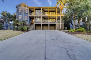 A two-story building with a balcony on the upper floor, a garage with two doors, and a driveway leading to the entrance. - Sunset Rentals | Four Thirty Third (Isle of Palms)