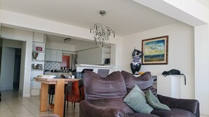 Un salon moderne avec un canapé marron, une table à manger et une cuisine en arrière-plan.