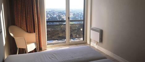 Une pièce comprenant un lit, une chaise et offrant une vue sur le paysage urbain grâce à une grande fenêtre.