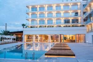 A modern hotel with a pool, multiple floors, and a well-lit entrance. - At Herbal Boutique Hotel & Spa (Paralimni)
