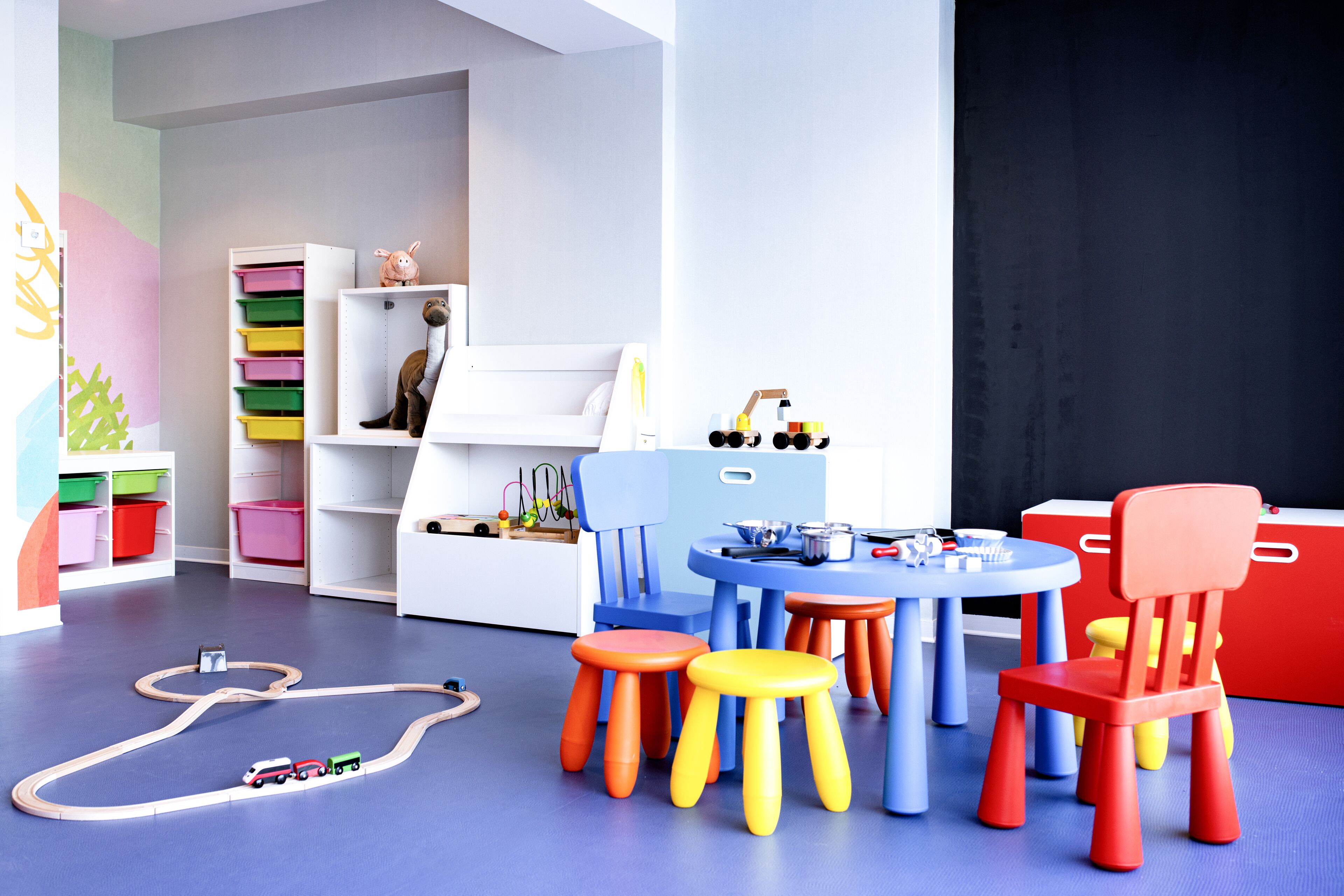 Un cuarto de juegos infantil con taburetes coloridos, una mesa de juegos y unidades de almacenamiento.