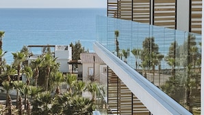 En moderne bygning med en glasbalkon med udsigt over et kystområde med palmer og havet.
