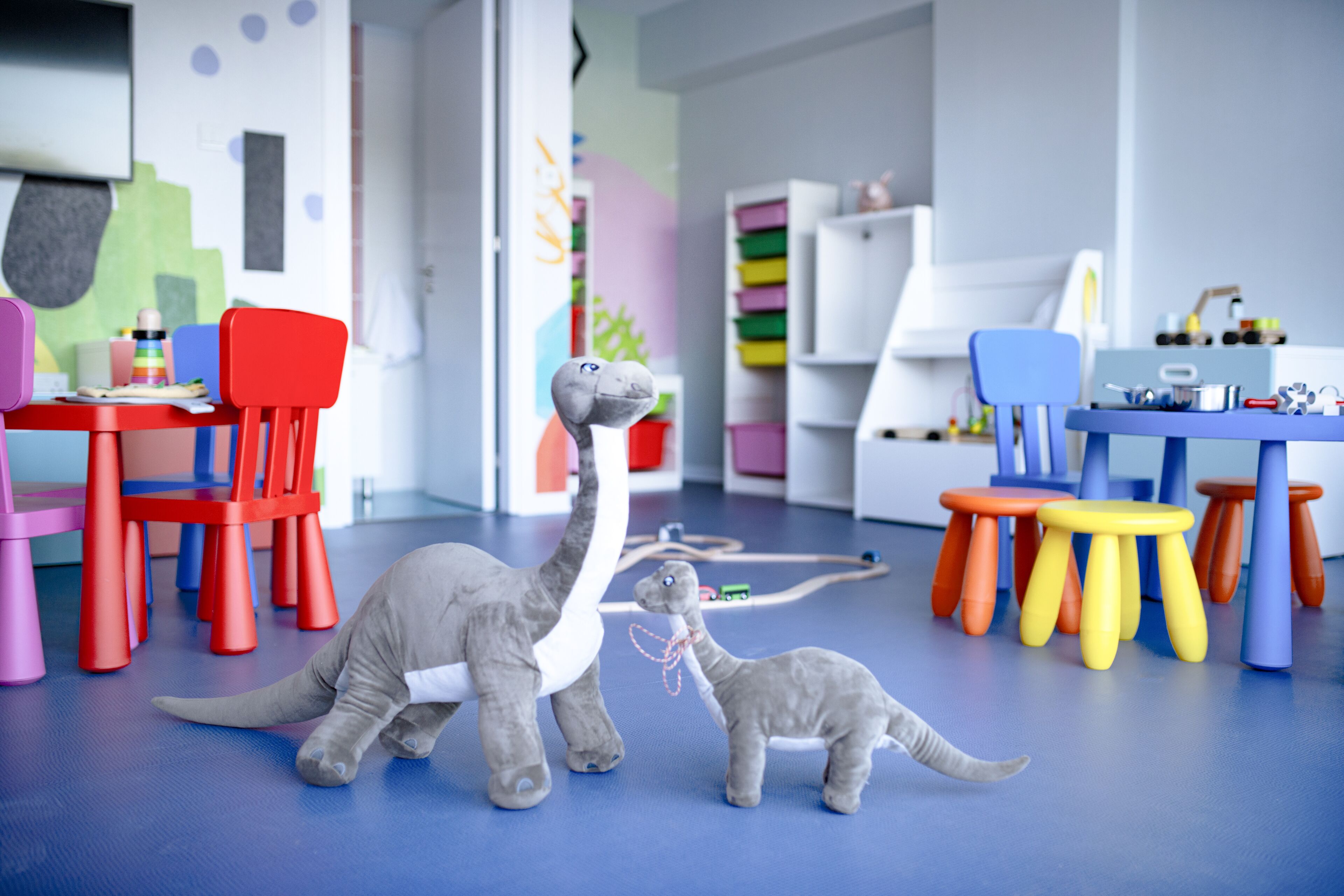 Una habitación con sillas coloridas, un juguete de dinosaurio y un suelo azul.