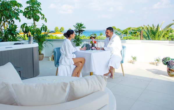 A couple seated at a table with a view of the sea, surrounded by potted plants and a spa area. - At Herbal Boutique Hotel & Spa (Paralimni)