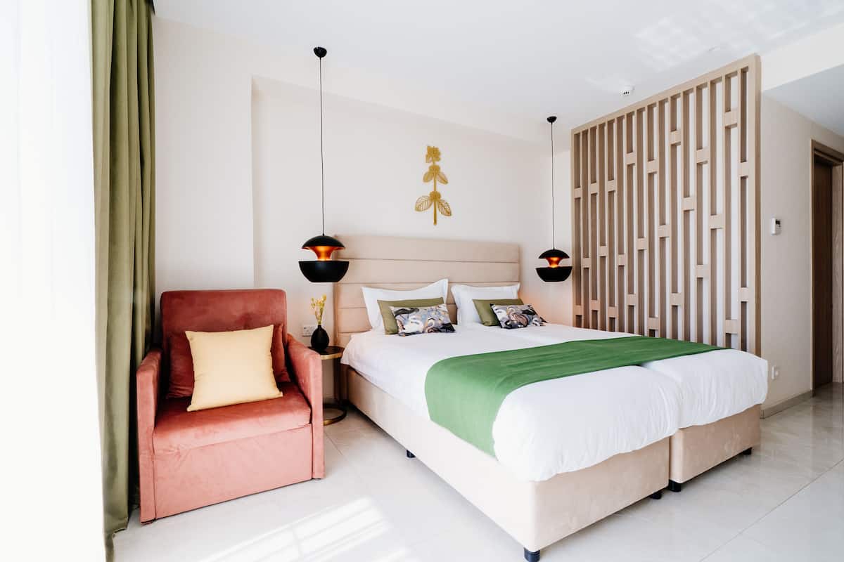 A modern hotel room with a bed, a red armchair, a nightstand, and a decorative wall piece.