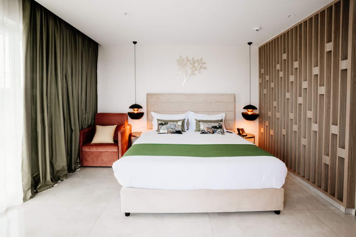 A modern bedroom with a large bed, a red chair, and a wooden panel wall.