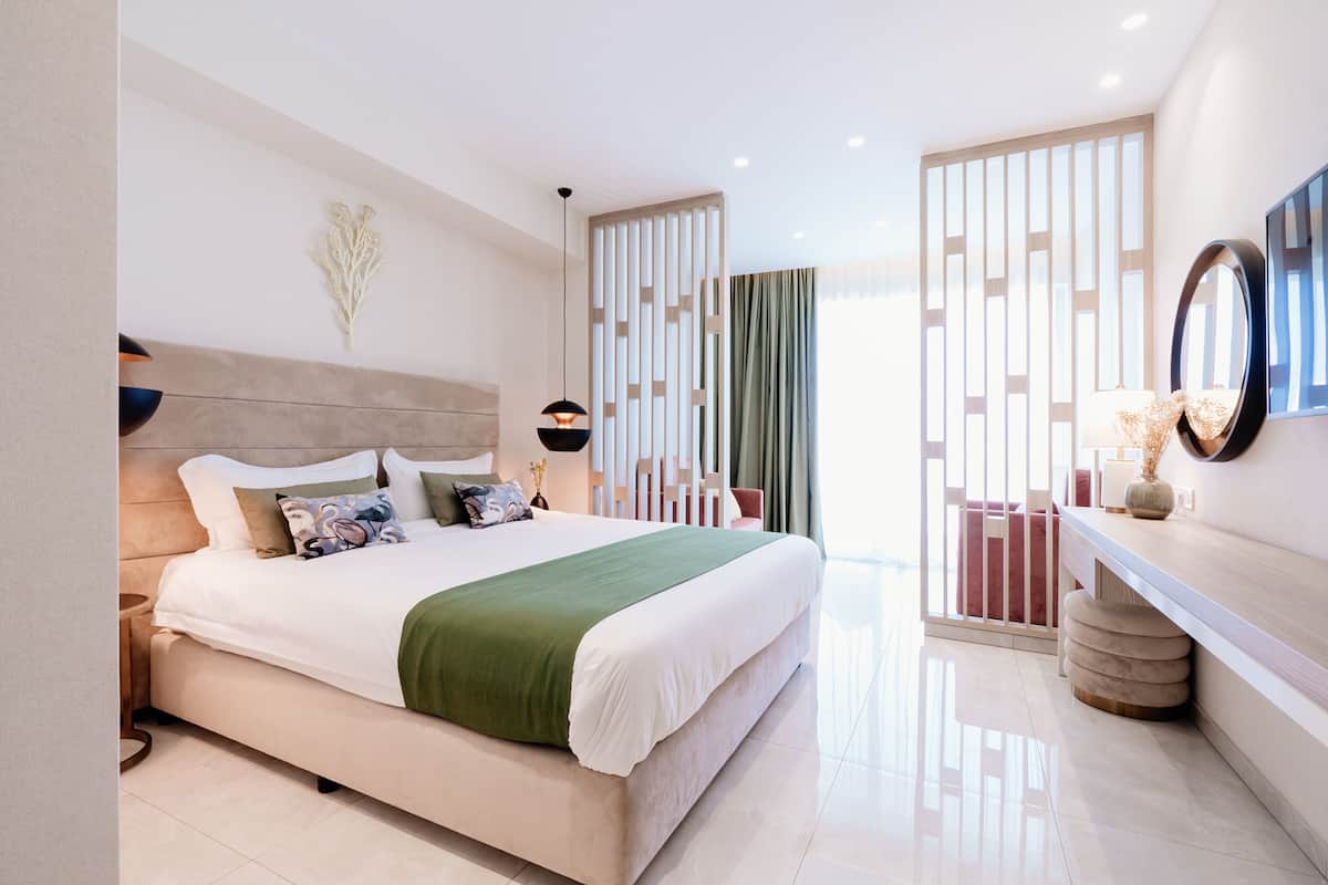 A modern bedroom with a large bed, bedside tables, a mirror, and a view through a window with curtains.