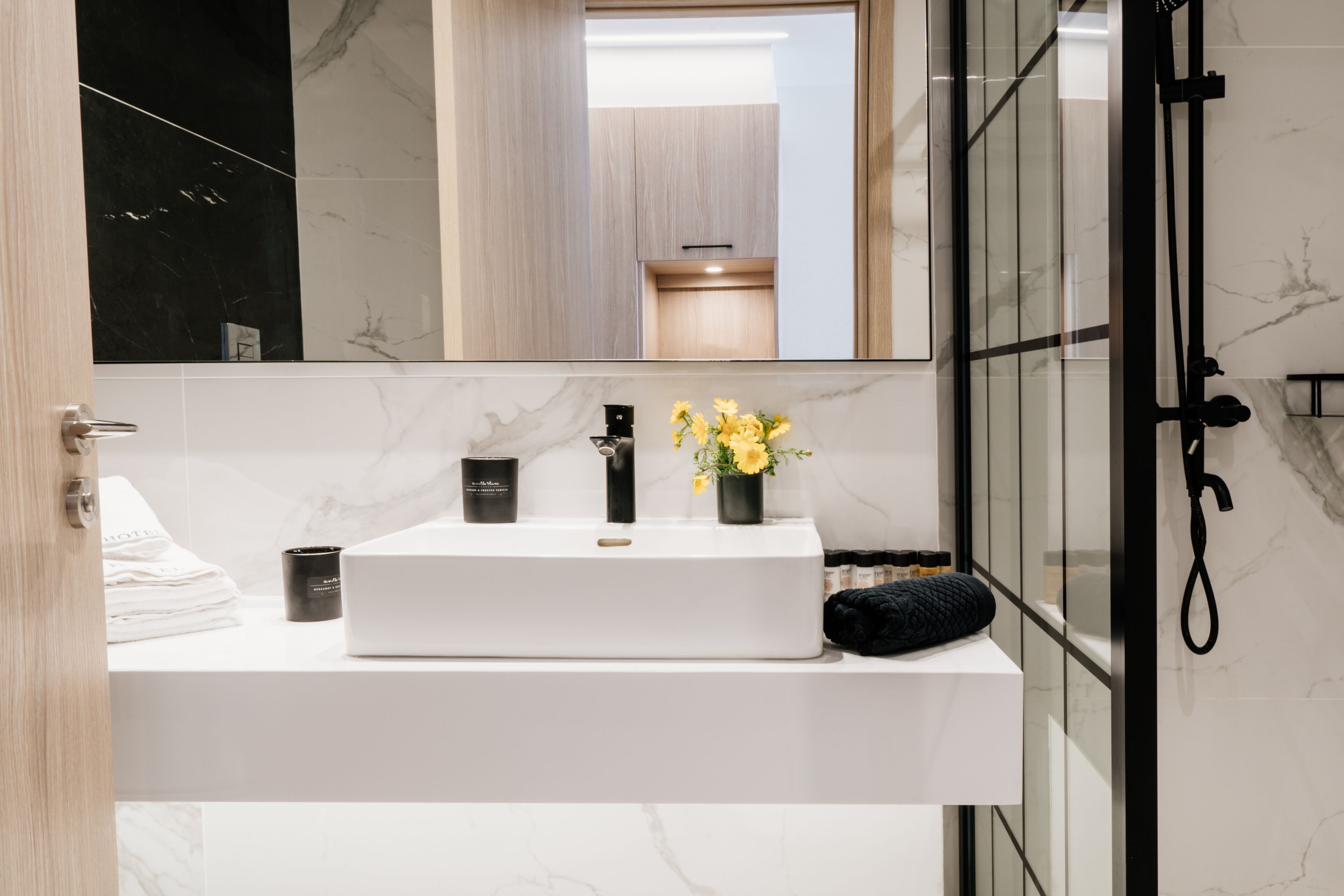 A modern bathroom with a white marble sink, a black faucet, and a mirror above it. There is a black towel and a black container on the sink.