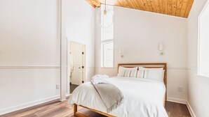 Une chambre avec un cadre de lit en bois, du linge de lit blanc, un tapis blanc et un plafond en bois.