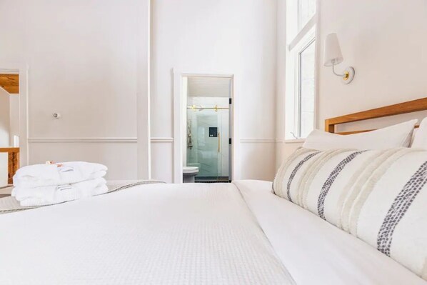 Habitación de hotel con una cama bien hecha, baño visible a través de una puerta abierta y ventana que proporciona luz natural.