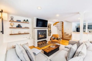 Cozy living space with a fireplace, comfortable seating, and a staircase leading upstairs.