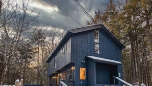 Une maison en bois à deux étages, à l’extérieur d’un bleu foncé, entourée d’un paysage enneigé et d’arbres.