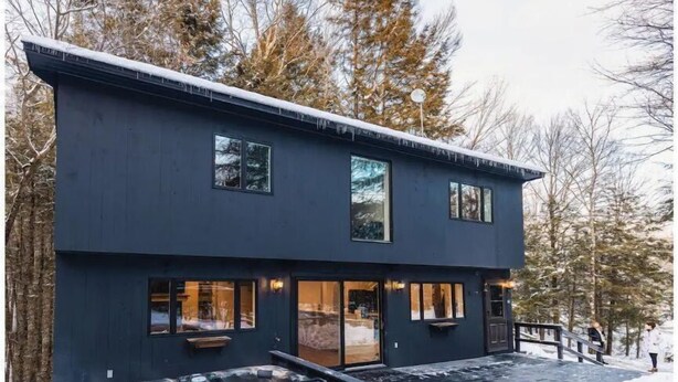 Un bâtiment moderne à deux étages, doté d’un jacuzzi à l’avant, entouré de neige et d’arbres.