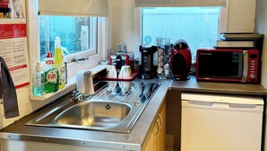 Une cuisine compacte équipée d’un évier en acier inoxydable, d’un four à micro-ondes rouge et noir, d’une machine à café et d’une fenêtre donnant sur la ville.