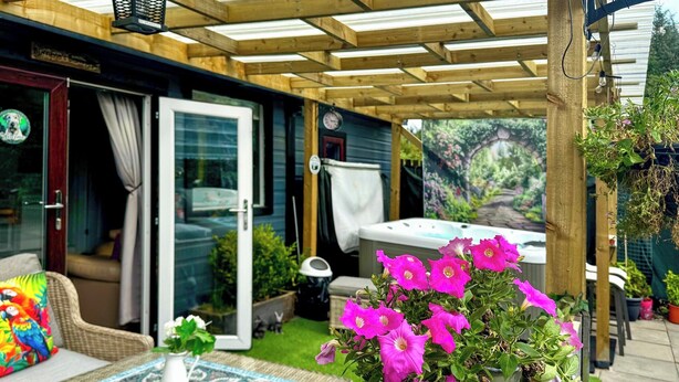 Un patio couvert avec une table en osier, un pot de fleurs orné de fleurs roses et un jacuzzi.