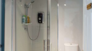 Une salle de bain moderne avec une douche à parois de verre, des toilettes et une petite étagère contenant des articles de toilette.