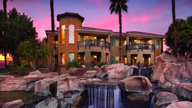 A hotel with a waterfall feature, multiple balconies, and a sunset view.