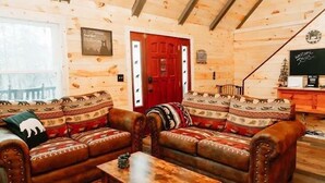 A log cabin interior with a leather sofa, a wooden coffee table, and a red door. - Luxury Vacation Mountain Home (Pickens)
