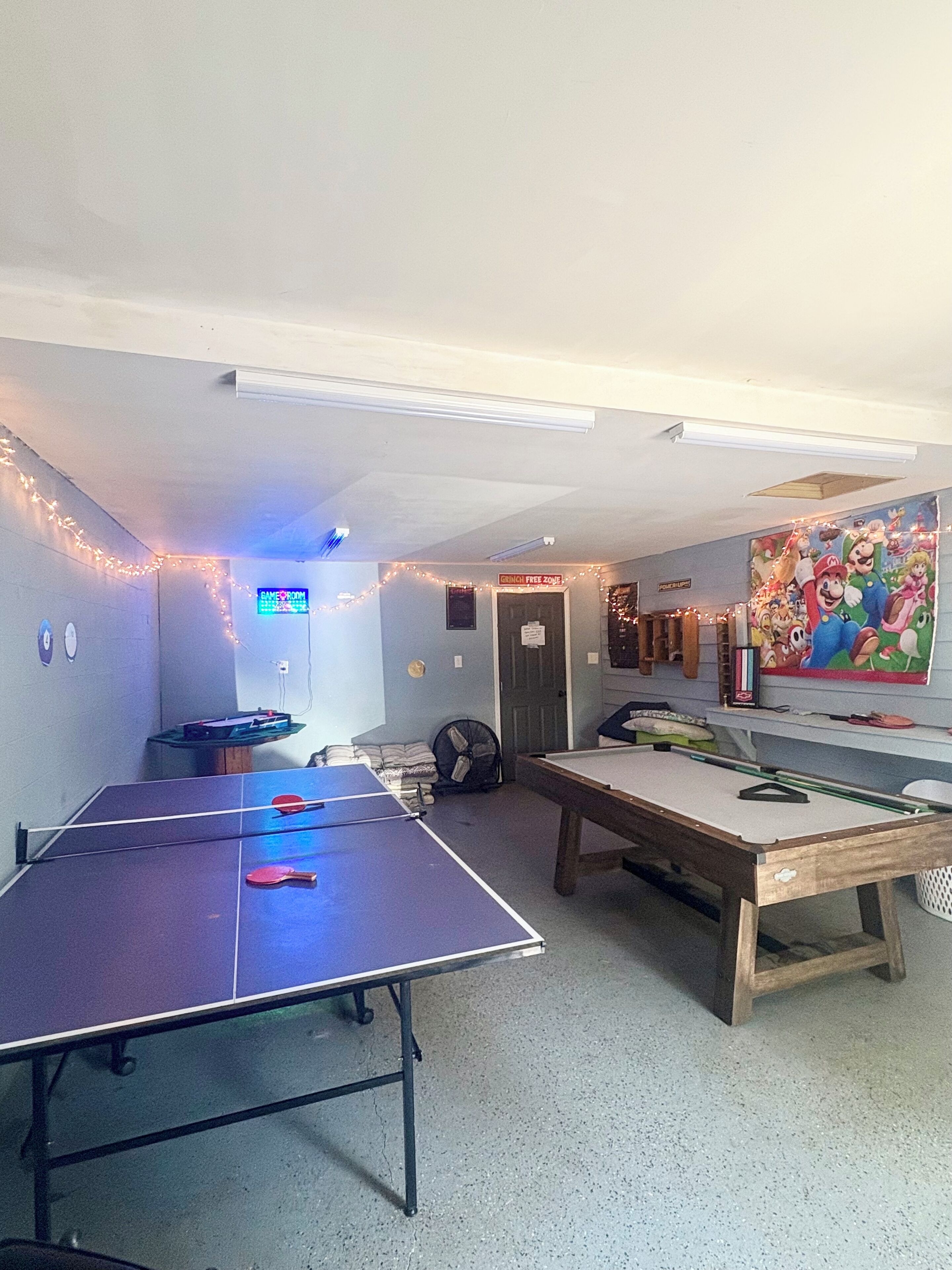 Une pièce équipée d’une table de ping-pong, d’un billard et d’un espace de jeux avec un panneau indiquant « Zone sans Grinch ».