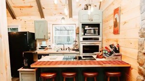 A wooden cabin interior with a kitchen area, bar stools, and a stone wall. - Luxury Vacation Mountain Home (Pickens)