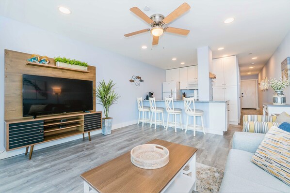 A modern living room with a flat-screen TV, wooden entertainment unit, and a ceiling fan. - Direct Oceanfront Villa / Heated Pool & Ocean View (Hilton Head Island)