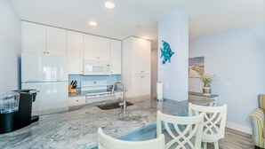 A modern kitchen with white cabinets, a marble countertop, a sink, and a dining area with white chairs. - Direct Oceanfront Villa / Heated Pool & Ocean View (Hilton Head Island)