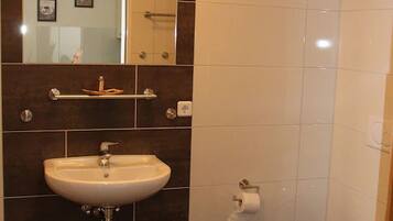 A bathroom with a dark tiled wall, a white sink, a mirror, a toilet, and a shelf with toiletries.