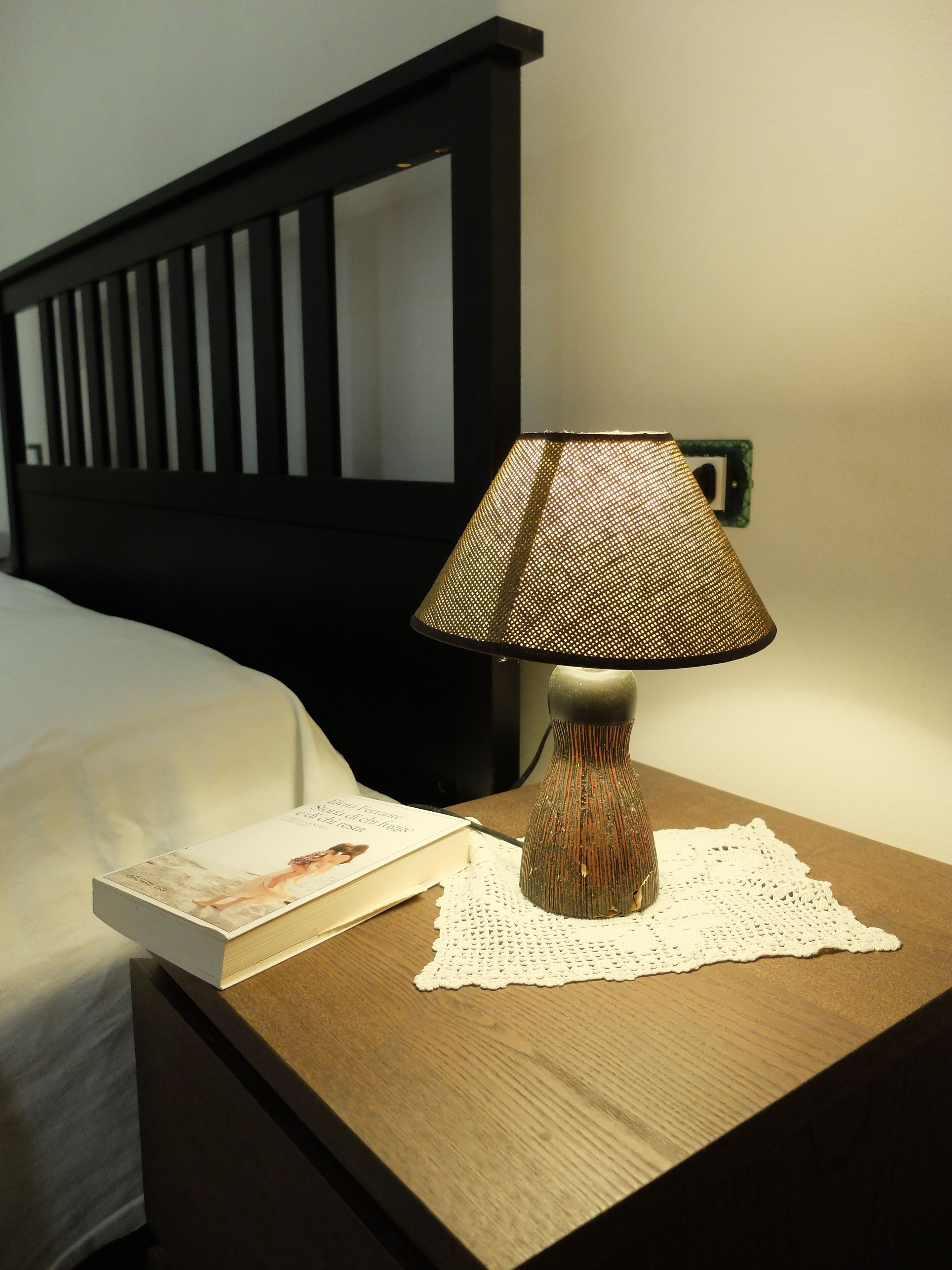A bedside table with a lamp, a book, and a doily.