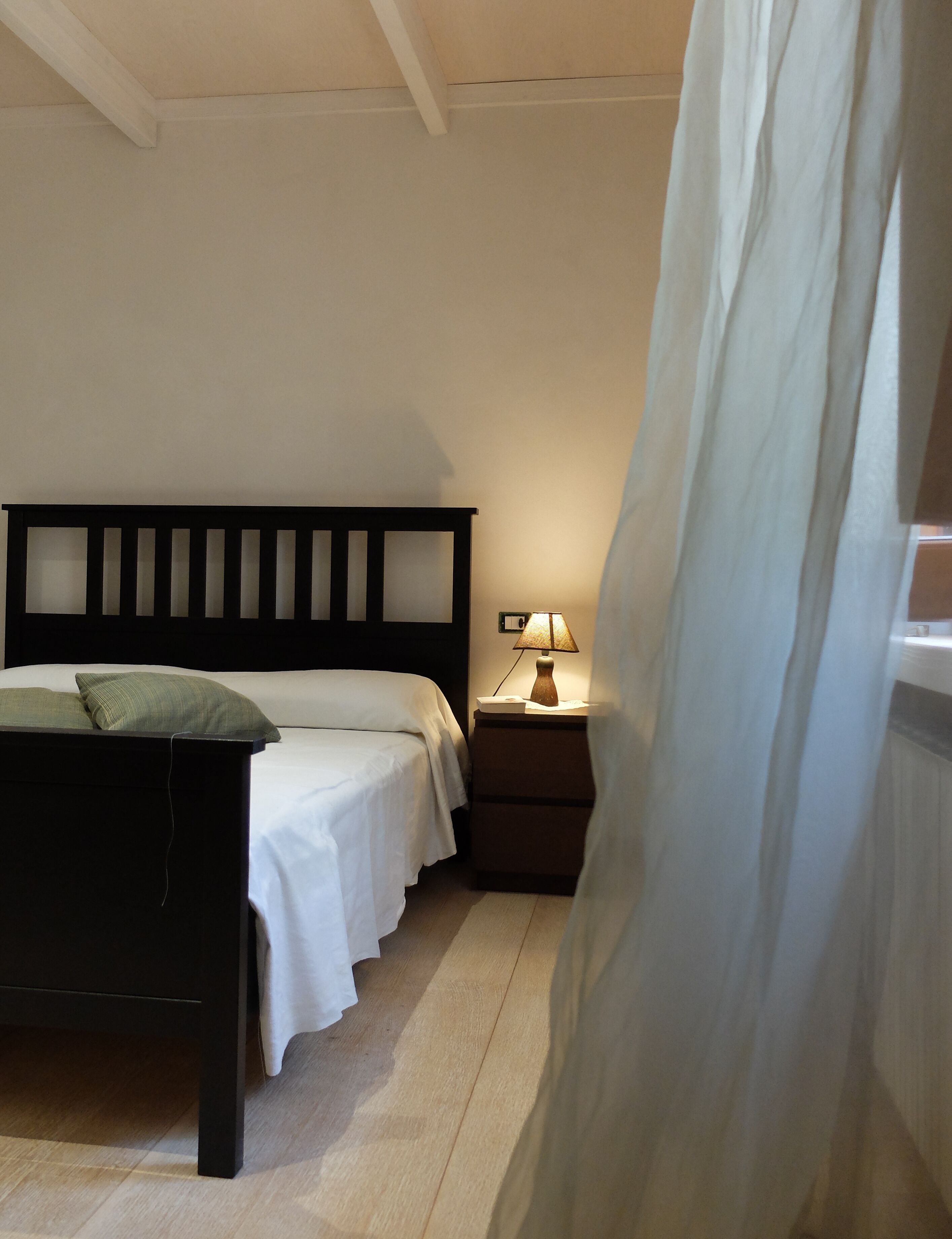 Una camera da letto con un letto, un comodino, una lampada e una tenda parzialmente aperta.