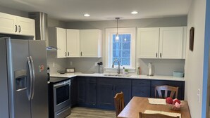Cocina moderna con refrigerador, horno y microondas integrados. Hay una mesa de comedor con sillas y una ventana sobre el fregadero.