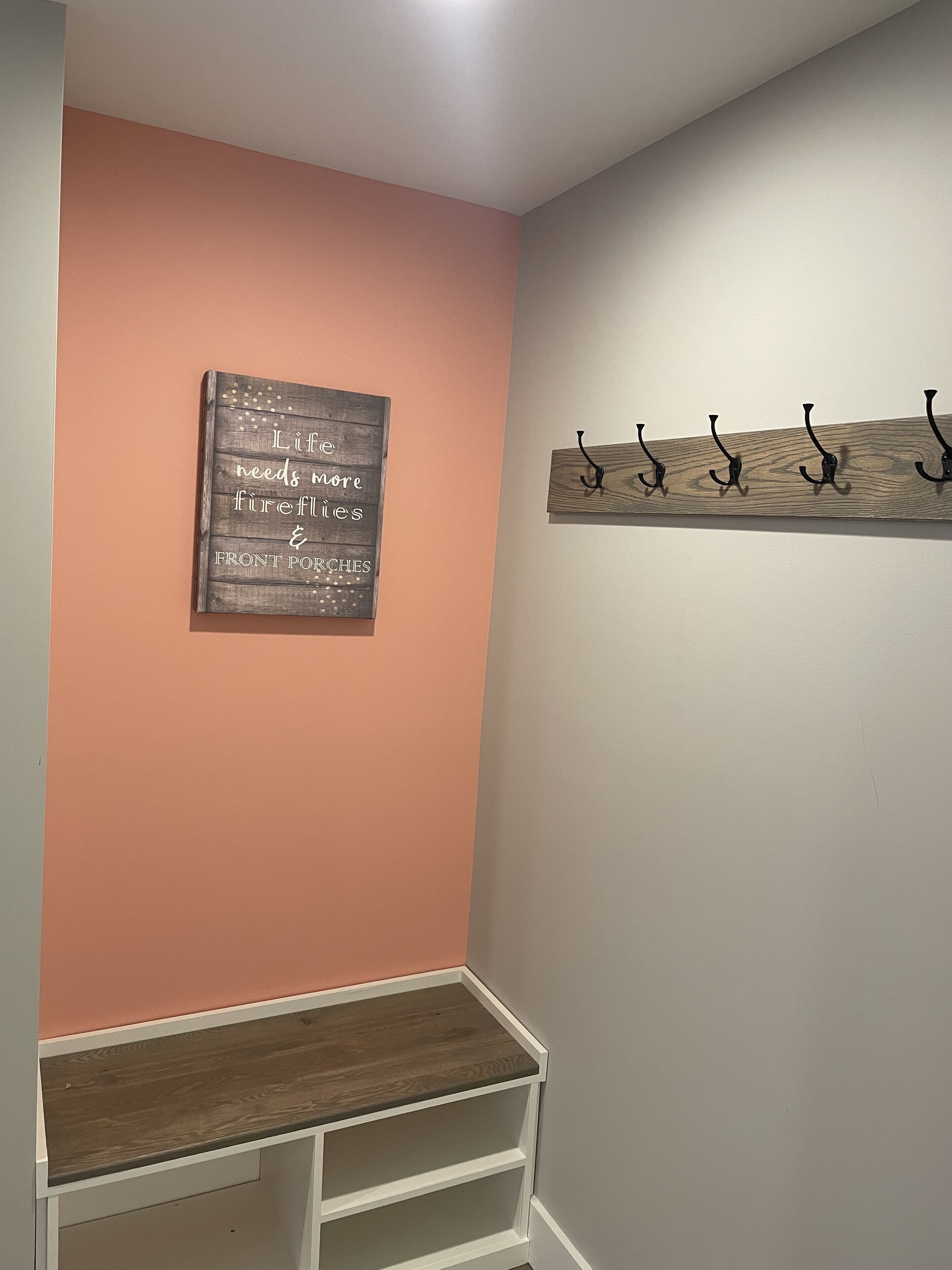 Una habitación con pared color melocotón, un letrero de madera con texto y una repisa de madera con ganchos.