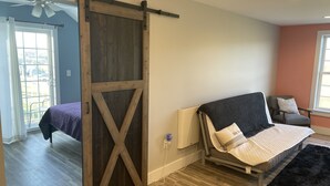 Un dormitorio con cama, sofá, puerta corrediza estilo granero y vistas a través de una ventana.