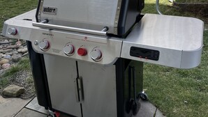 Una parrilla Weber Genesis portátil con cuatro quemadores, una repisa lateral y una chimenea.