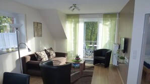 Una sala moderna con sofá, sillones, una mesa de centro y un balcón con vista a árboles.