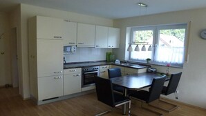 Una cocina moderna con armarios blancos, una mesa de comedor con sillas y un ventanal con cortinas.