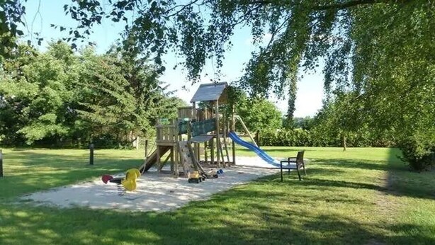 Estructura de juego de madera con un tobogán, rodeada de césped y árboles.