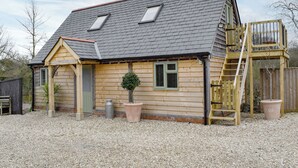 Ein Holzhaus mit geneigtem Dach, zwei Dachfenstern, einer Holztreppe und einem eingezäunten Spielbereich.