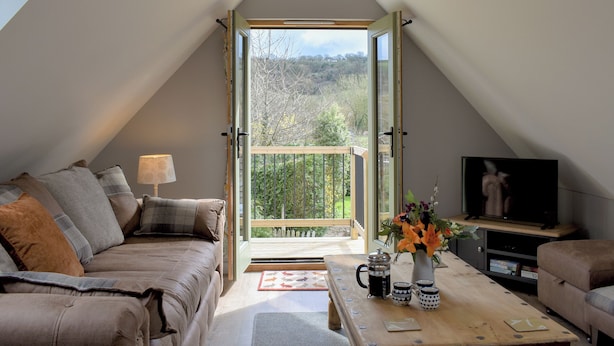 Ein gemütliches Schlafzimmer im Loft-Stil mit einem großen Oberlicht, einer Couch, einem Couchtisch mit Blumenvase und einem Fernseher auf einem Holzboden.