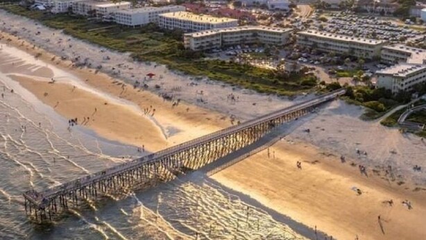 Un hotel frente al mar con vista a la playa, un muelle y un puerto deportivo al fondo.