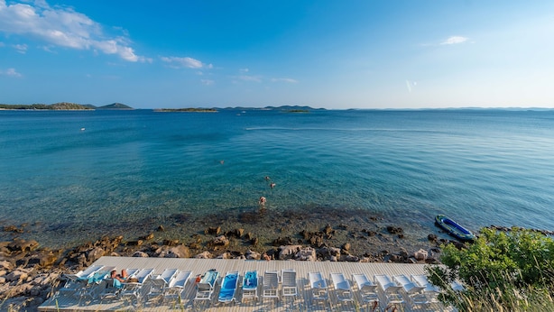 A beachside view with clear waters, a wooden deck with sun loungers, and distant islands. - Mobile Home Pecten Exclusive 2 (Pakostane)