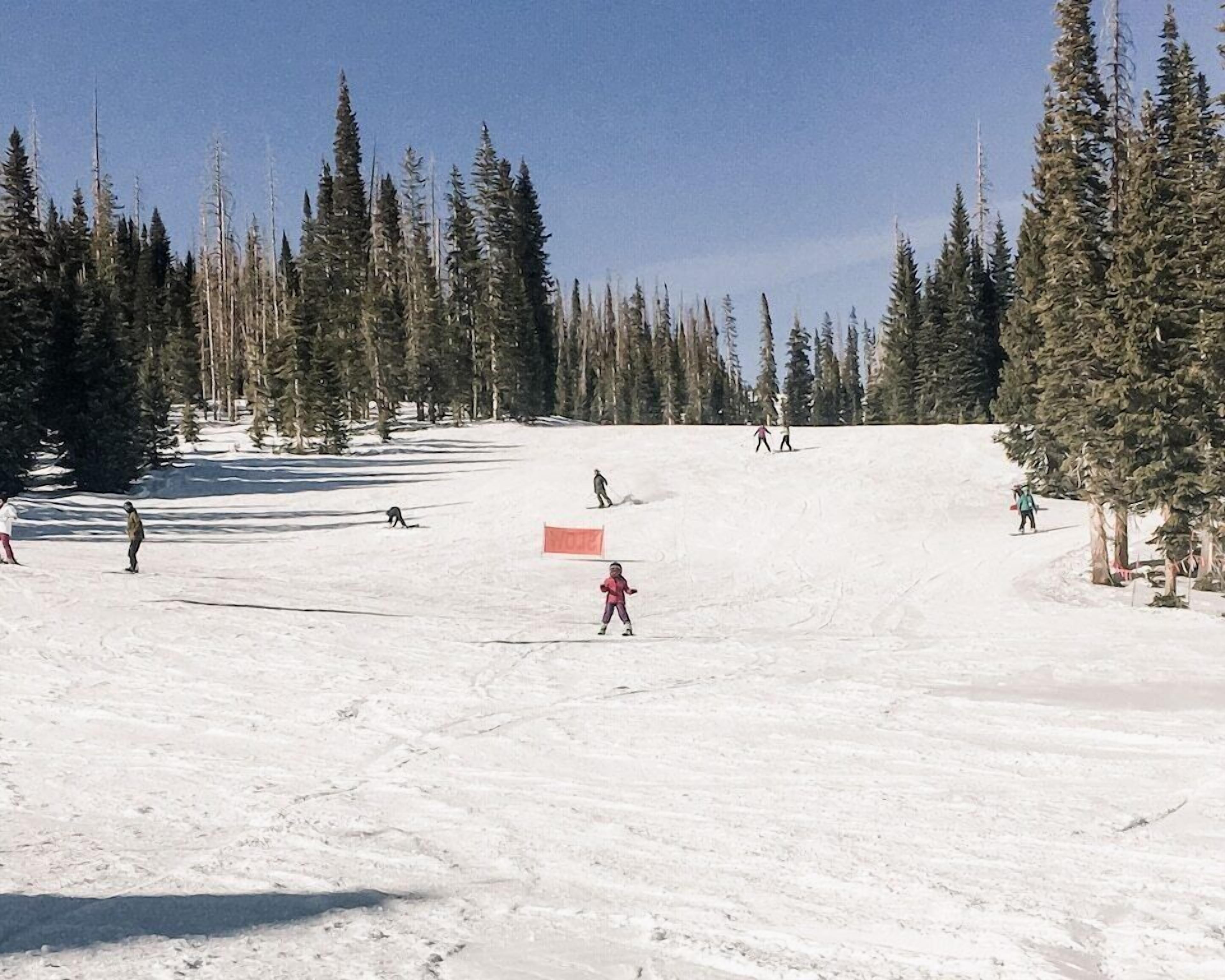 A snowy ski slope with skiers and a red sign.