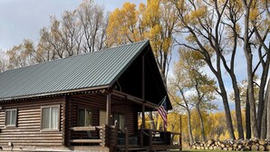 Een rustieke blokhut met veranda, een pad van baksteen dat ernaar leidt en een stapel hout op de achtergrond.
